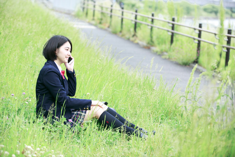 フリー写真 草むらに座って携帯電話で話ししている女子高生