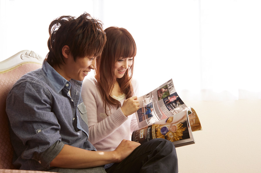 フリー写真 ソファーに座って雑誌を見ているカップル